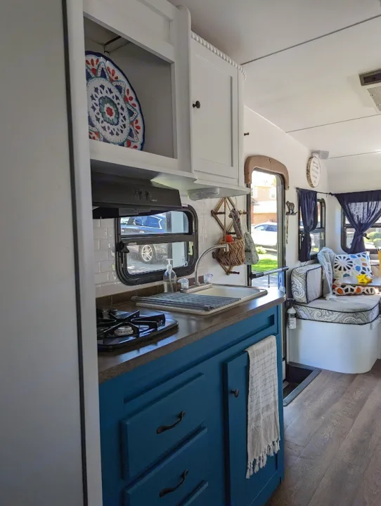 Inside an RV rental: a compact kitchen with teal cabinets, stove, and sink, next to a comfy dining bench with pillows.. Gulf Stream Vista Cruiser M-19RSD 2013