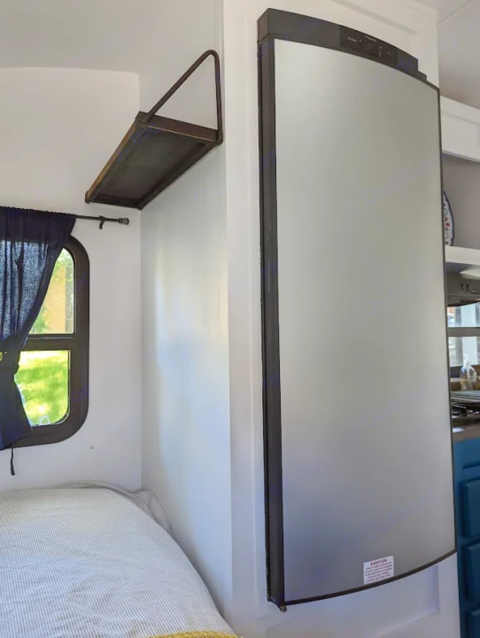 A cozy RV rental interior with a striped bed, window, wall shelf, and a sleek silver Dometic refrigerator/freezer on the right.. Gulf Stream Vista Cruiser M-19RSD 2013