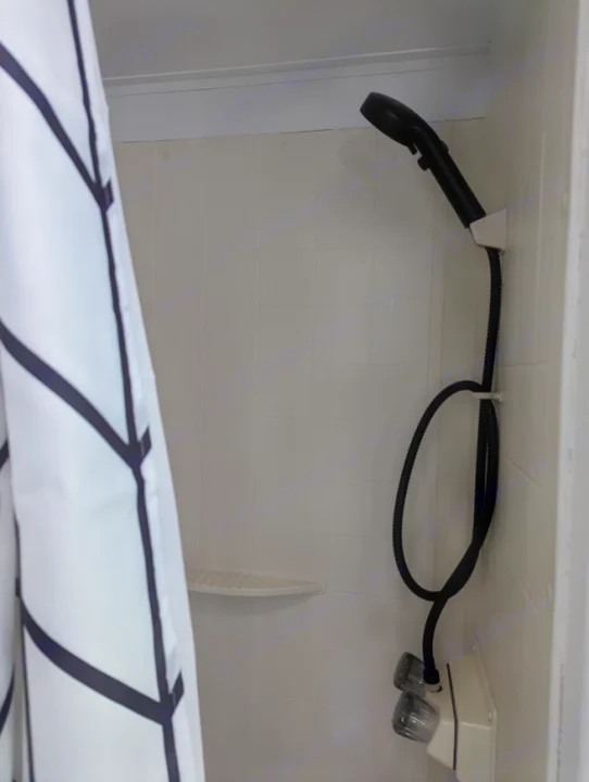 Compact RV rental shower: white stall, black handheld head, dual controls, and a small corner shelf. Curtain visible.. Gulf Stream Vista Cruiser M-19RSD 2013