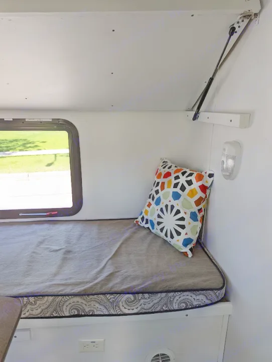 RV rental interior: A cozy bench/bed with patterned cushion, colorful pillow, a window view, and overhead storage support.. Gulf Stream Vista Cruiser M-19RSD 2013