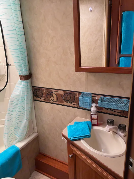 A compact RV rental bathroom featuring a sink, mirror, shower/tub with curtain, and vibrant blue towels and organizers.. Holiday Rambler Campmaster 2011