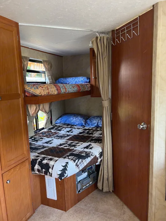 Cozy RV rental interior featuring comfortable bunk beds with windows, wooden cabinetry, and a private door, ideal for family travel.. Holiday Rambler Campmaster 2011