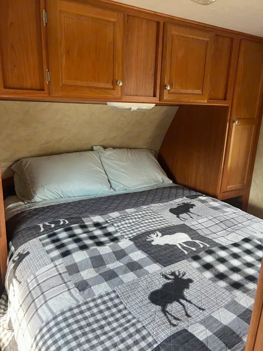 RV rental bedroom: gray and white plaid moose comforter, two pillows, and wood cabinets.. Holiday Rambler Campmaster 2011