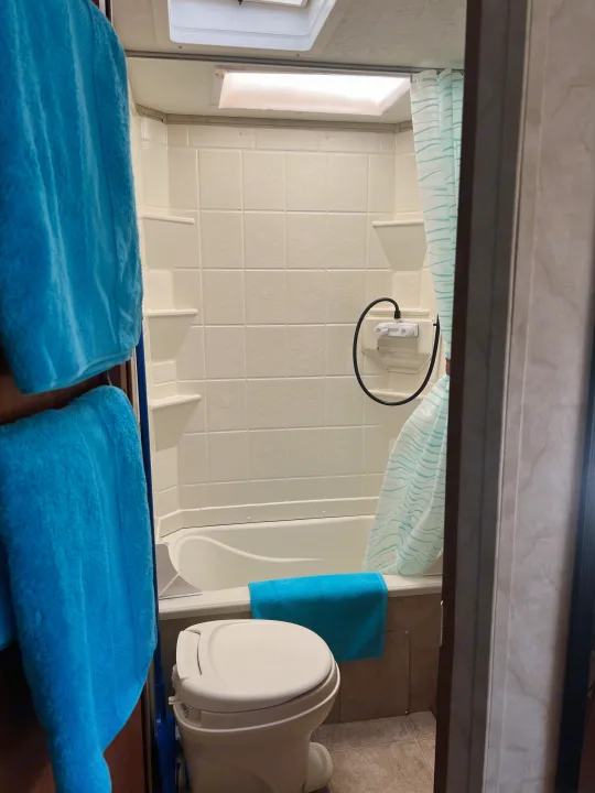 Inside an RV rental: a compact bathroom with a toilet, small tub/shower, blue towels, and a ceiling vent.. Holiday Rambler Campmaster 2011