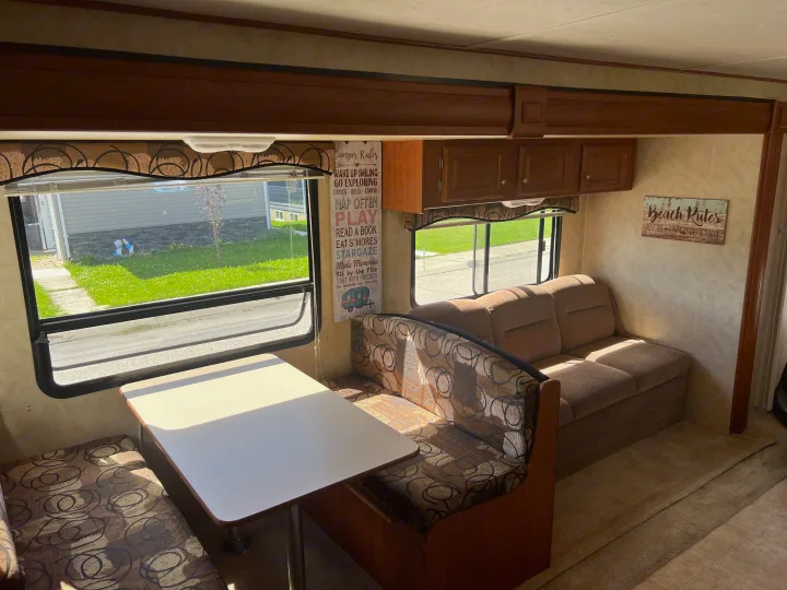 Cozy rv rental interior featuring a bright dinette, comfy sofa, and large windows with an outdoor view.. Holiday Rambler Campmaster 2011