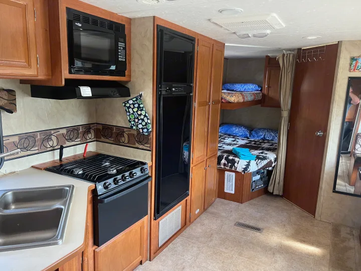 Inside this RV rental: A compact kitchen with microwave, stove, sink, refrigerator, and comfortable bunk beds for travel.. Holiday Rambler Campmaster 2011