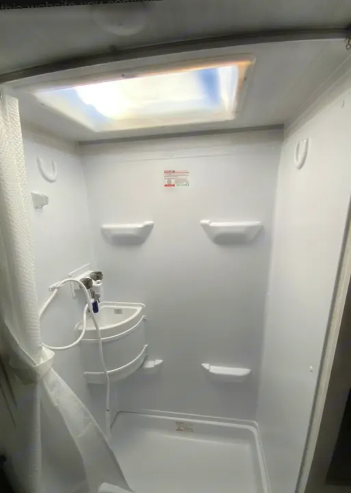 RV rental's compact all-white shower, featuring a corner sink with hose shower head, shelves, and a skylight.. Forest River R POD 193  H.R. EDITION 2022
