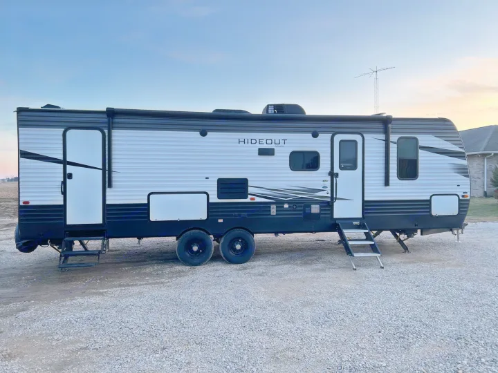 Hideout rv rental, white and black, parked on gravel, awaits your next road trip or camping adventure.. Keystone Hideout 2020