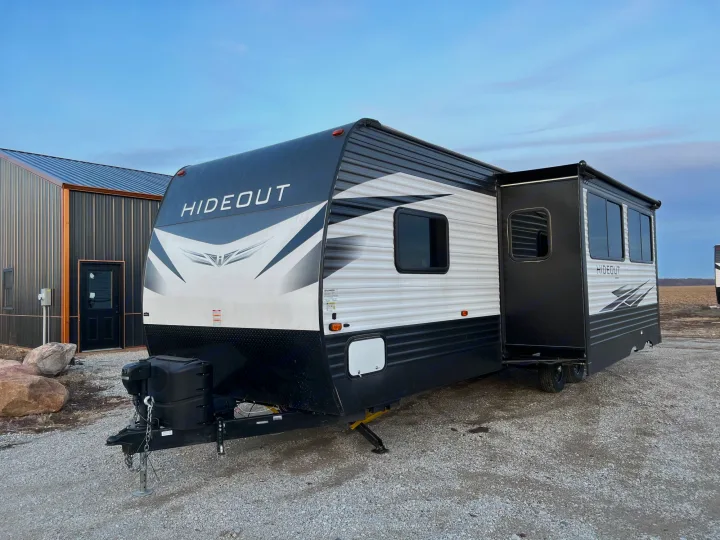 A sleek black and white Hideout travel trailer, ideal for an RV rental, parked on gravel with a building nearby.. Keystone Hideout 2020