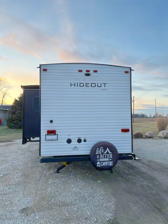 This Hideout RV rental, a white travel trailer, is parked on gravel at sunset, ready for your camping trip.. Keystone Hideout 2020