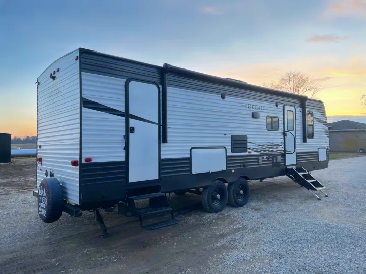 A sleek "Hideout" travel trailer RV rental, parked on gravel at sunset, awaits your next camping adventure.. Keystone Hideout 2020