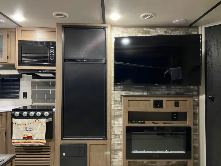 This RV rental interior features a compact kitchen with stove, microwave, and fridge, plus a TV and electric fireplace for comfort.. Keystone Hideout 2020