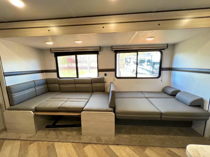 Inside an RV rental: a flexible U-shaped dinette with grey cushions that converts into a large bed, ideal for trips.. Crossroads Zinger 2023