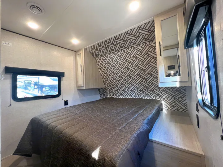 Inside an **rv rental**: a modern bedroom with a comfortable bed, stylish geometric accent wall, and bright windows.. Crossroads Zinger 2023