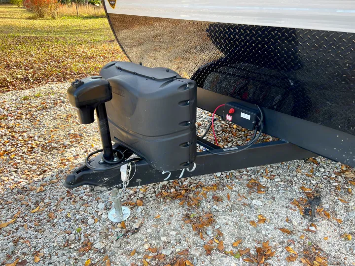 Detailed view of an RV rental travel trailer's front, highlighting the hitch, power jack, covered propane tanks, and battery system.. Crossroads Zinger 2023