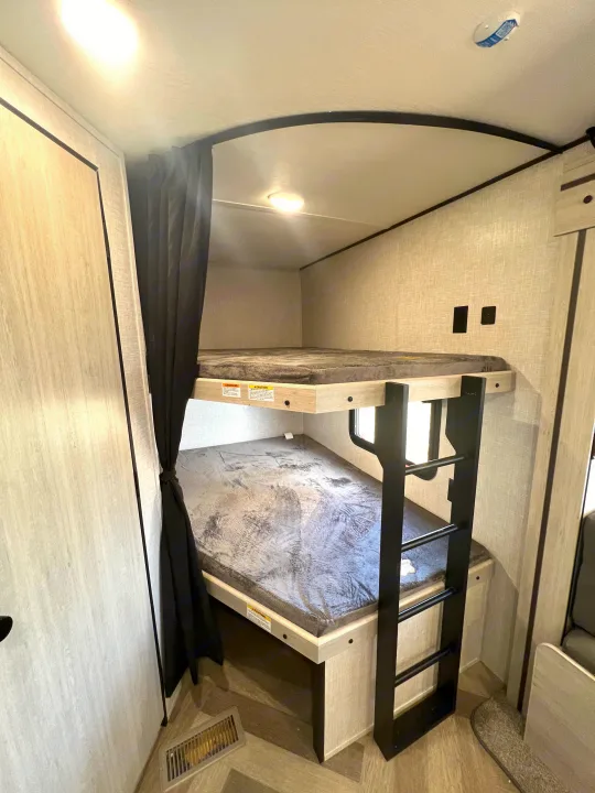 Comfortable bunk beds with ladder and privacy curtains in this RV rental, offering cozy sleeping space for guests.. Crossroads Zinger 2023
