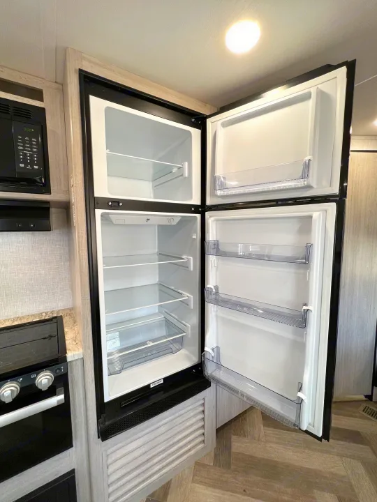 Inside an RV rental, a clean, open refrigerator with clear shelves and door bins awaits your provisions for travel.. Crossroads Zinger 2023