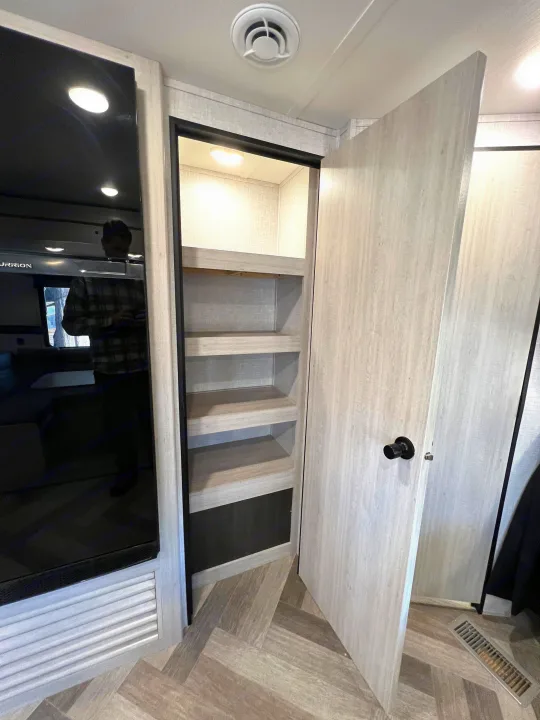 Inside this RV rental: view of a sleek TV, open pantry shelving, and light wood interior with herringbone flooring.. Crossroads Zinger 2023