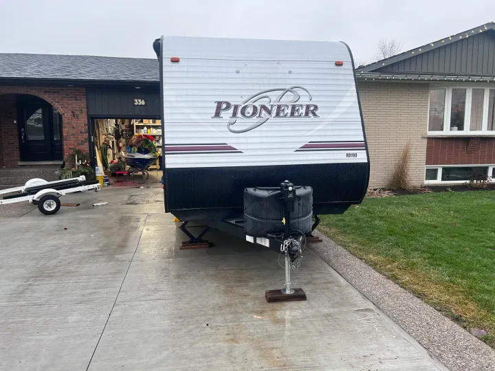 A large white Pioneer travel trailer is parked on a wet concrete driveway in front of a house, perfect for RV rental.. Heartland RVs Pioneer 2016