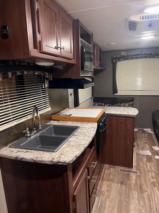 An RV rental's interior, showcasing a practical kitchen with sink, stove, microwave, and a cozy dinette area.. Heartland RVs Pioneer 2016