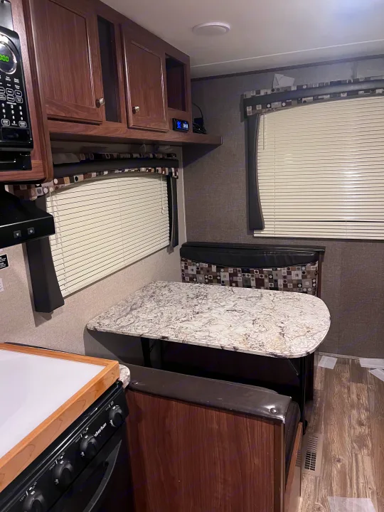 Cozy RV rental interior with kitchen, microwave, dining booth, and cabinets. Ideal for comfortable travel adventures.. Heartland RVs Pioneer 2016