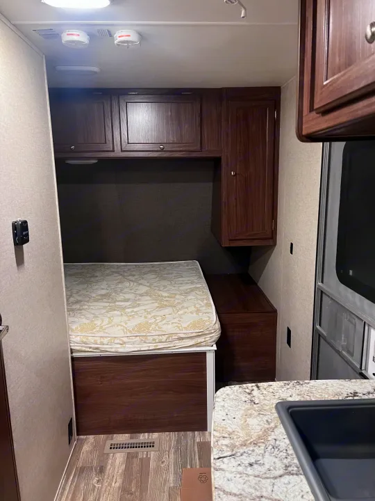 Cozy RV rental bedroom featuring a comfortable bed, built-in storage cabinets, and overhead safety devices.. Heartland RVs Pioneer 2016