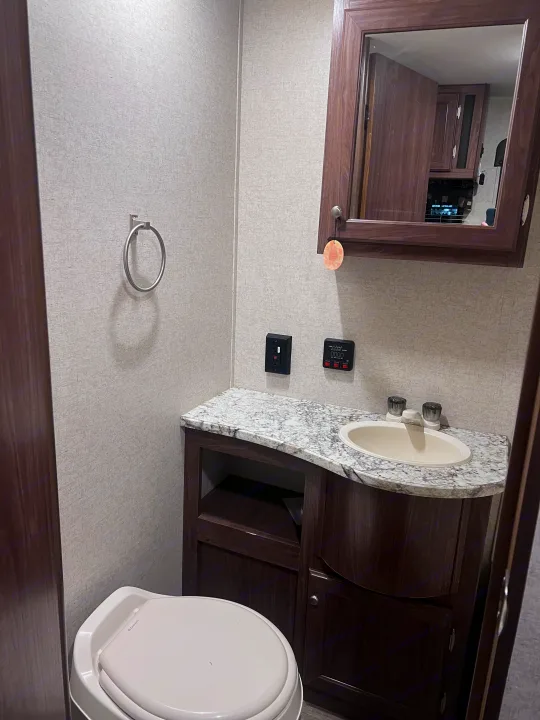 Compact RV rental bathroom with toilet, vanity, sink, and mirror. Note the tank level monitor and towel ring for convenience.. Heartland RVs Pioneer 2016