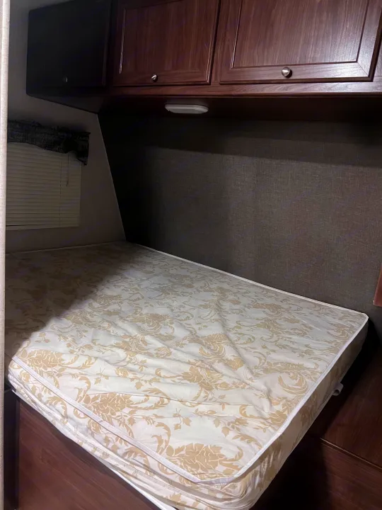 RV rental bed with white & tan floral mattress, dark wood cabinets, and window blinds. A cozy sleeping area for travel.. Heartland RVs Pioneer 2016