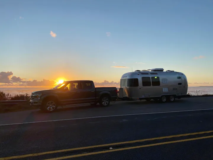 Sunset over the ocean with a truck towing an Airstream trailer. An ideal RV rental for scenic adventures!. Airstream Flying Cloud 2017