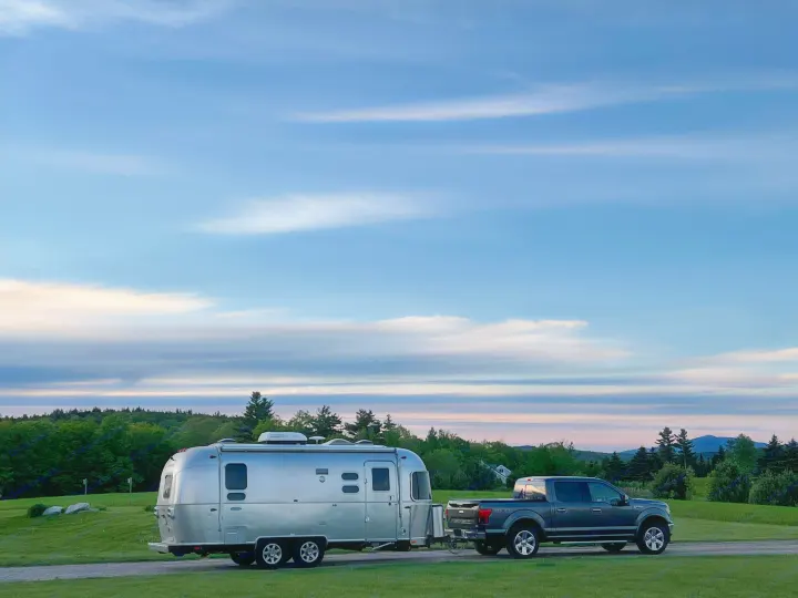 A shiny Airstream RV rental towed by a pickup truck, parked in a scenic natural landscape at dawn/dusk, perfect for camping.. Airstream Flying Cloud 2017