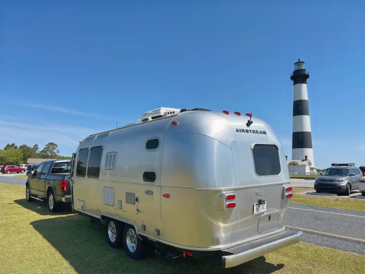 Silver Airstream RV rental & truck parked at a lighthouse with black & white stripes against a clear blue sky.. Airstream Flying Cloud 2017
