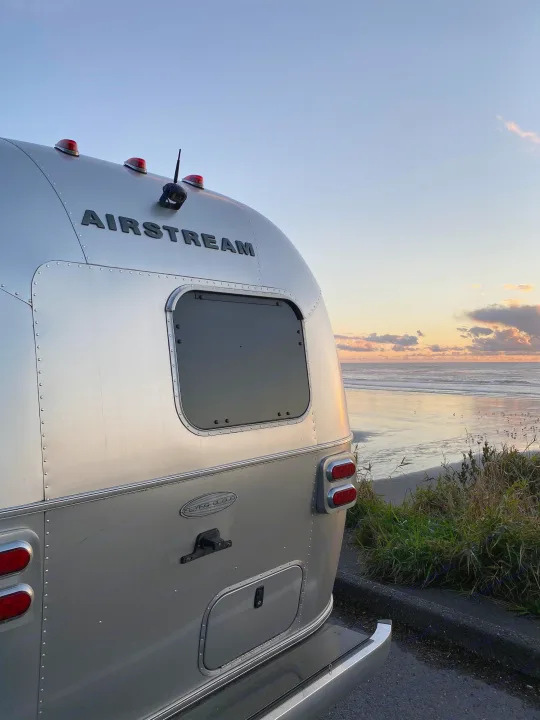 An iconic Airstream RV rental overlooks a serene beach and ocean at sunset, offering a unique travel experience.. Airstream Flying Cloud 2017