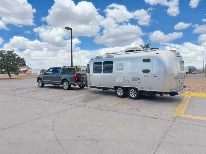Dark gray truck tows a shiny Airstream RV rental in a parking lot under a blue sky with clouds. Ready for a road trip.. Airstream Flying Cloud 2017