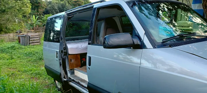 Converted van ready for your next rv rental adventure! Open doors reveal a cozy bed inside, parked in a lush outdoor setting.. Chevrolet Astro 2000