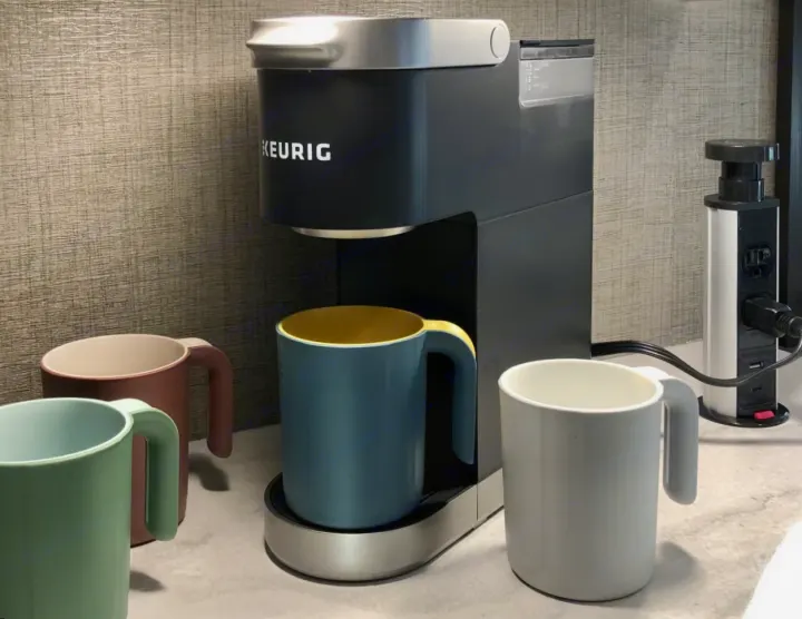 An RV rental kitchen shows a black Keurig coffee maker, colorful mugs, and a power strip for appliances.. Jayco Redhawk 2023