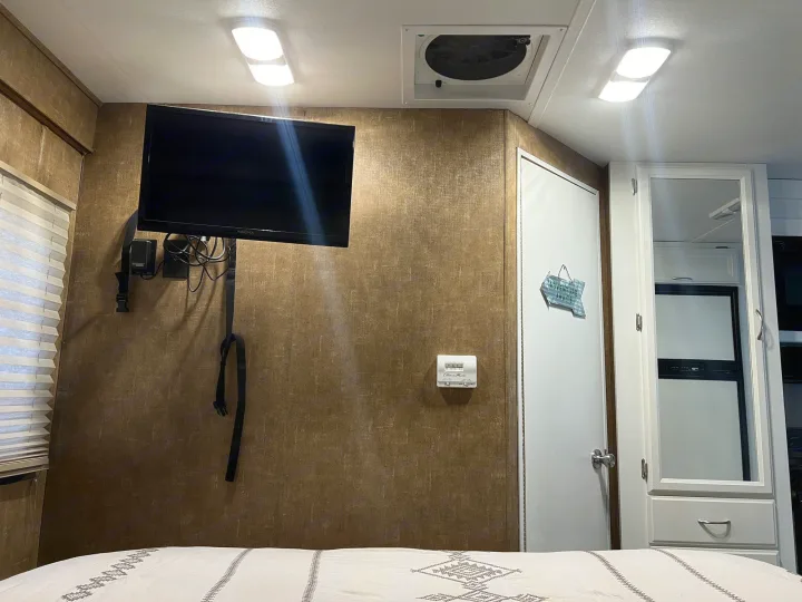 An RV rental's cozy interior features a mounted TV, thermostat, and mirrored storage, ready for new adventures.. Thor Four Winds 2014