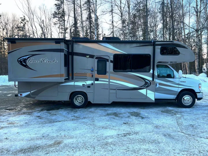 This Four Winds RV rental, a Class C motorhome, is parked on snowy ground against bare trees.. Thor Four Winds 2014
