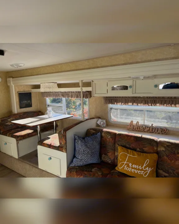 Cozy RV rental interior featuring a floral dining booth, comfortable seating, and bright windows, ideal for travel adventures.. Starcraft Antigua 2007