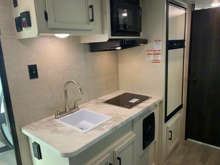 Compact RV rental kitchen with sink, microwave, cooktop, and refrigerator. Ideal for mobile living.. Jayco Jay Flight SLX 2022