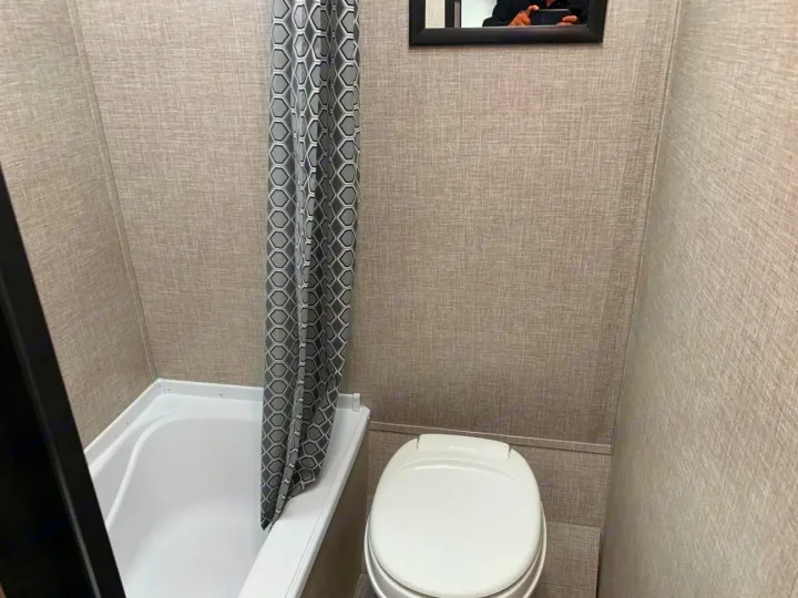 Inside an RV rental: a compact bathroom with a white tub, geometric shower curtain, and toilet, showing efficient use of space.. Jayco Jay Flight SLX 2022