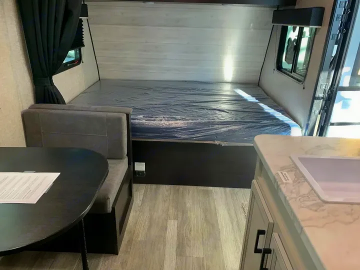 Clean RV rental interior featuring a bed with plastic cover, dinette seating, and kitchen area with a sink.. Jayco Jay Flight SLX 2022