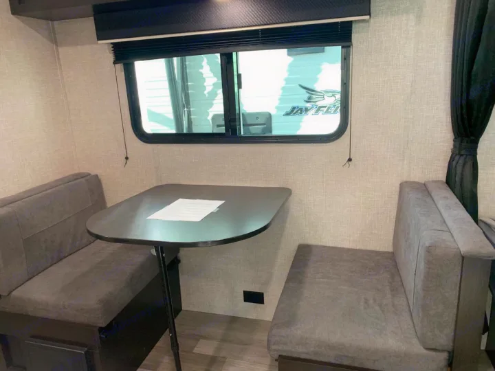 This RV rental features a cozy dinette area with a dark table, grey benches, and a window for scenic views.. Jayco Jay Flight SLX 2022