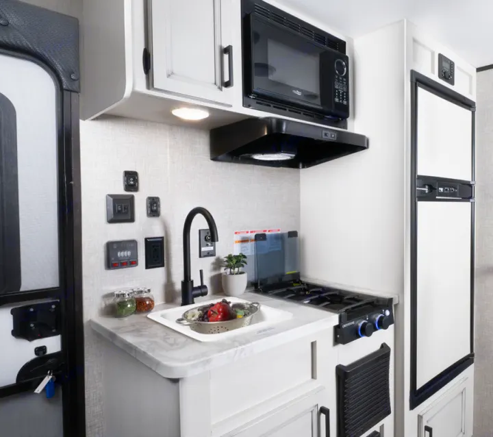 An RV rental's bright kitchen: sink, stovetop, microwave, fridge, and wall controls for comfortable travel cooking.. Jayco Jay Flight SLX 2022