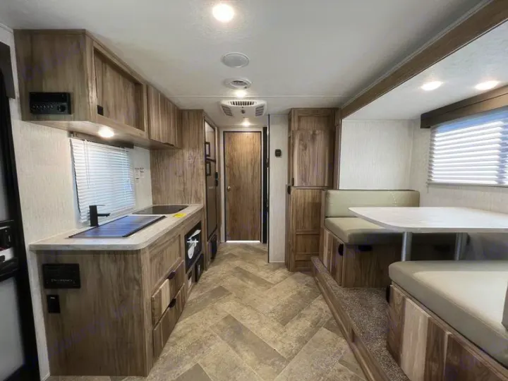 An RV rental's sleek interior, featuring a compact kitchen counter, sink, stovetop, and comfortable dinette.. Forest River Palomino Palomini 2022