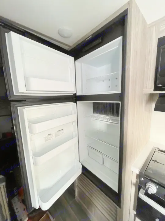 Clean Dometic refrigerator inside an RV rental. Top freezer, clear shelves, and door storage are visible in the compact kitchen.. Keystone Passport 2022