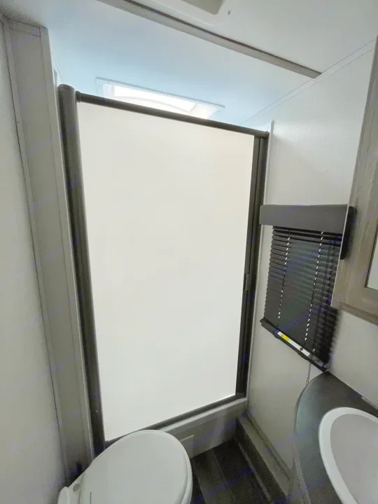 RV rental bathroom with skylight, featuring a compact toilet, retractable shower screen, and window blinds.. Keystone Passport 2022