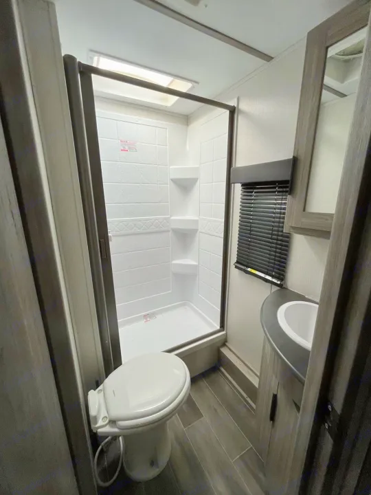 Compact RV rental bathroom: white toilet on left, glass shower center, sink vanity on right.. Keystone Passport 2022