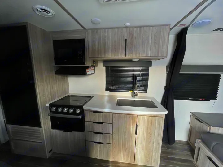 Modern RV rental interior with a fully equipped compact kitchen (stove, sink, microwave, fridge) and cozy dining area.. Keystone Passport 2022