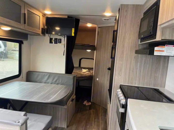 Inside an **rv rental**: functional kitchen, dining booth, TV, and bunk beds offer a cozy, versatile living space.. Keystone Passport 2022