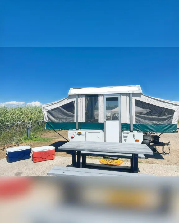 Pop-up camper, picnic table, and coolers at a sunny campsite. Consider an RV rental for your next trip!. Fleetwood Other 2005